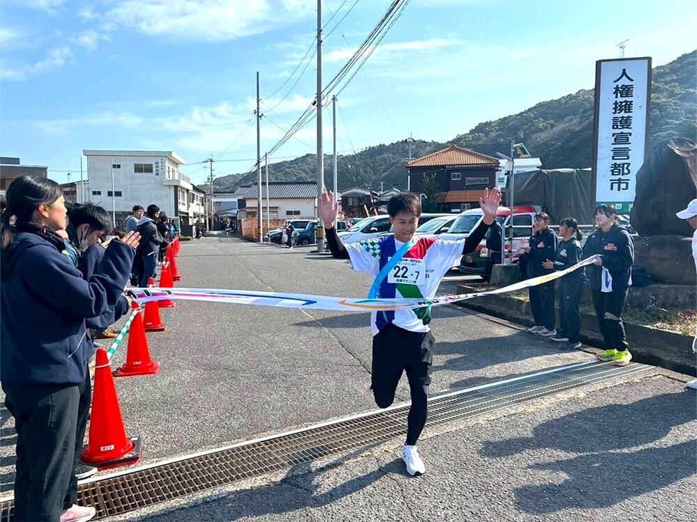 両手を上げ、ゴールテープを切る高知銀行のマラソン部員の写真/室戸岬一周駅伝